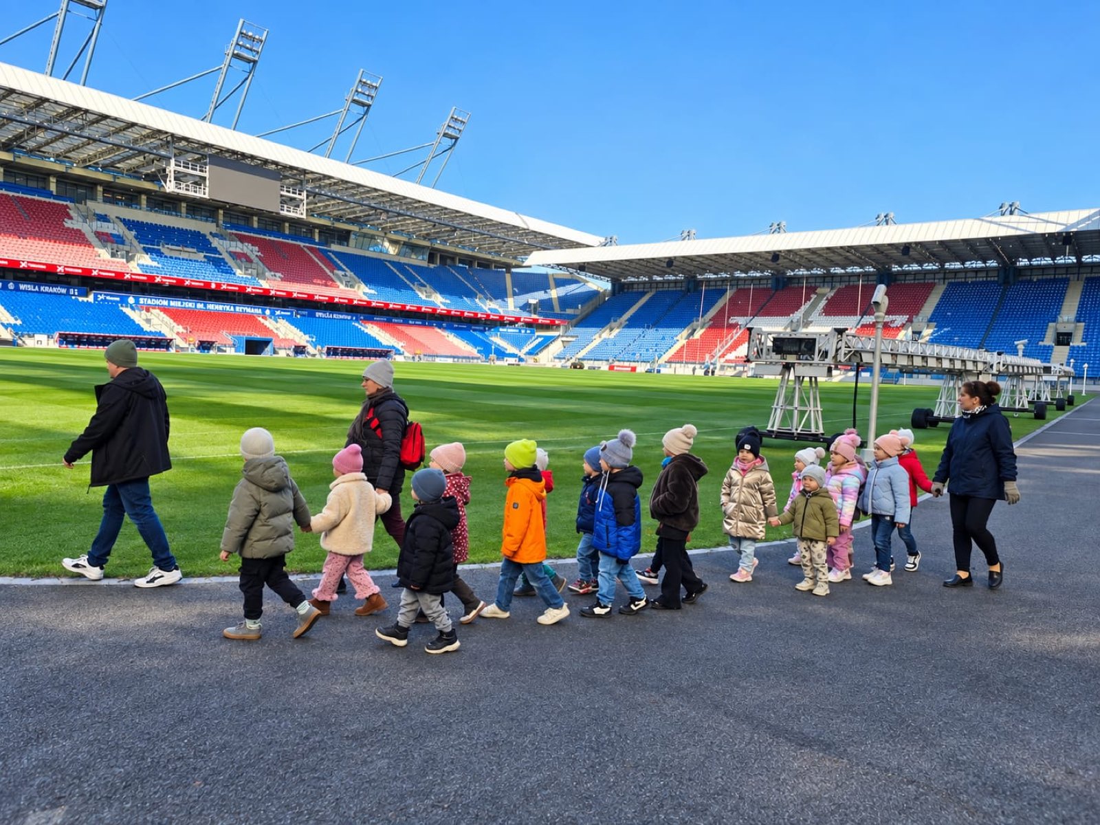 Grupa przedszkolaków idzie wzdłuż płyty boiska na Stadionie Miejskim Wisły Kraków